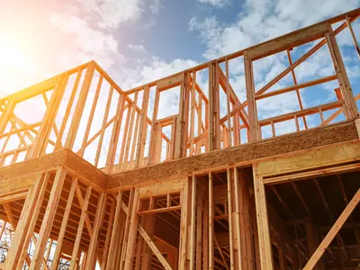 The framing of a house under construction against the backdrop of a cloud blue sky.