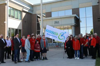 County of Essex employees and Accessibility Advisory Committee members and others in red shirts raise an Accessibility flag at the County of Essex Administration Building.