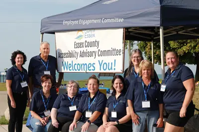Members of the Essex County Accessibility Advisory Committee wearing blue shirts in front of a blue tent and a welcome sign.