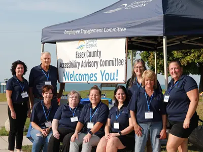 Members of the Essex County Accessibility Advisory Committee wearing blue shirts in front of a blue tent and a welcome sign.