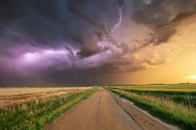 Lightning in a stormy sky above a dirt road in a rural area.