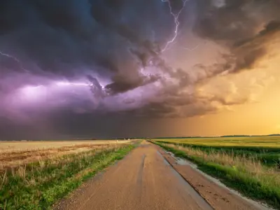 Lightning in a stormy sky above a dirt road in a rural area.