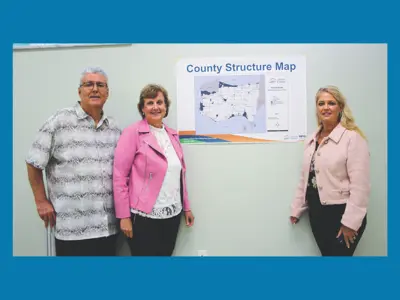 Rebecca Belanger and Mary Lou Tanner and Larry Silani pose by a map on a wall. 