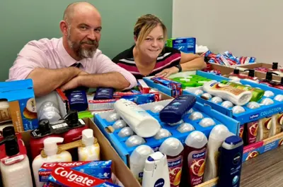 Adam Craig and Jeanie Diamond-Francis pose with boxes of toiletries collected by library staff. 