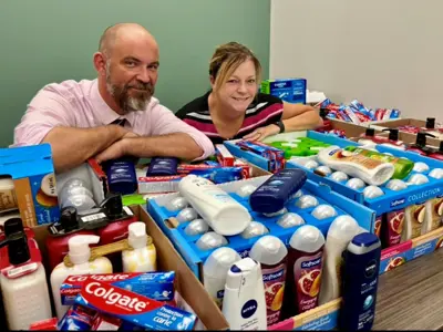 Adam Craig and Jeanie Diamond-Francis pose with boxes of toiletries collected by library staff. 