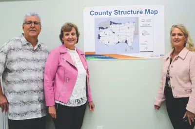 Rebecca Belanger and Mary Lou Tanner and Larry Silani pose by a map on a wall. 
