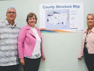 Rebecca Belanger and Mary Lou Tanner and Larry Silani pose by a map on a wall.