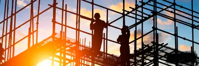 A worker on scaffolding against the setting sun.