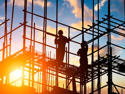 A worker on scaffolding against the setting sun.