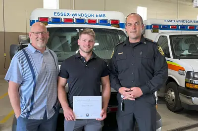 Survivor Greg Kempe with Ethan Muxlow and Chief Justin Lammers in front of an ambulance.